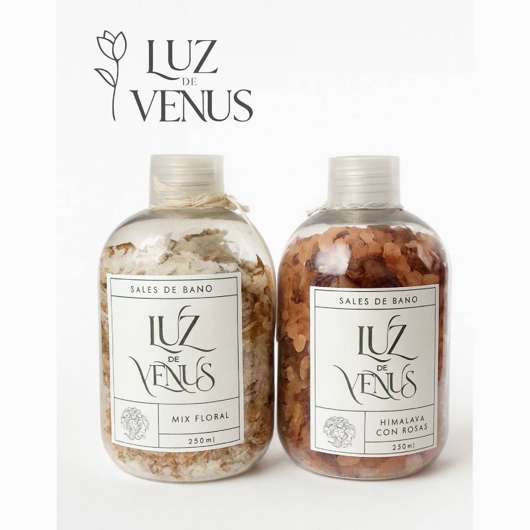 Dos botellas transparentes de sales de baño Luz de Venus, una beige y otra marrón, con el logotipo encima.