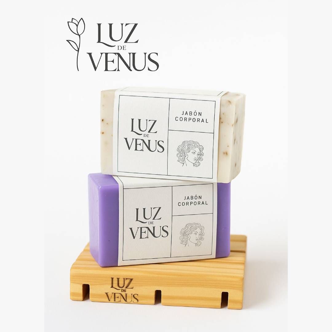 Dos pastillas de jabón Luz de Venus, una lavanda y otra color blanco roto, sobre una jabonera de madera.