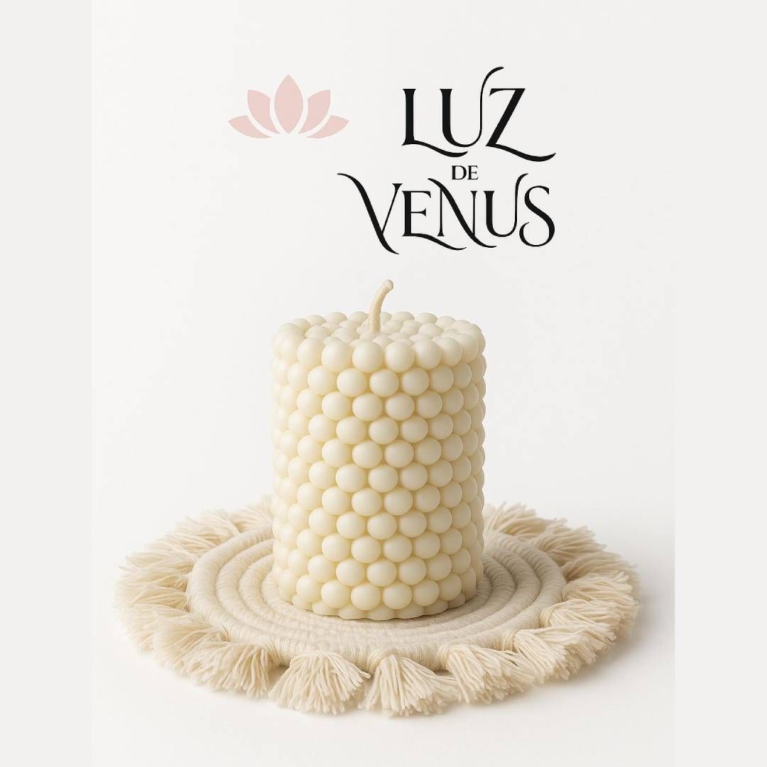 Una vela texturizada de color crema sobre un posavasos tejido, con las palabras "Luz de Venus" encima.