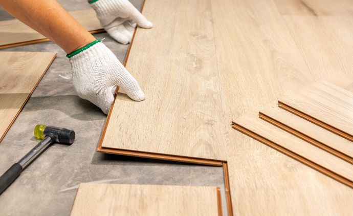 A person is installing a wooden floor with a hammer.