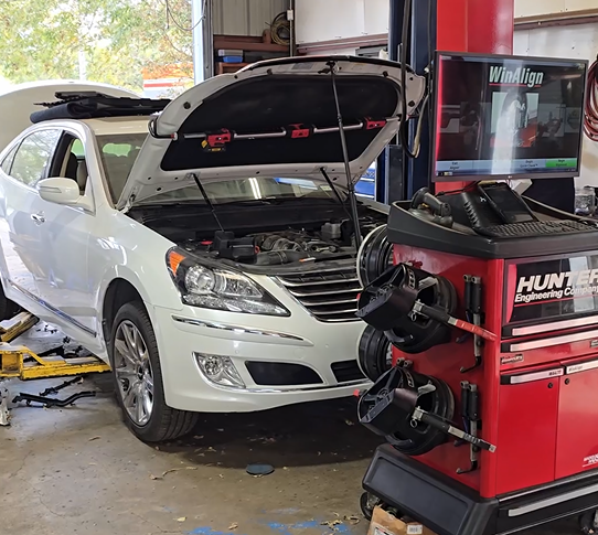 A white car is sitting on a lift in a garage with its hood open.
