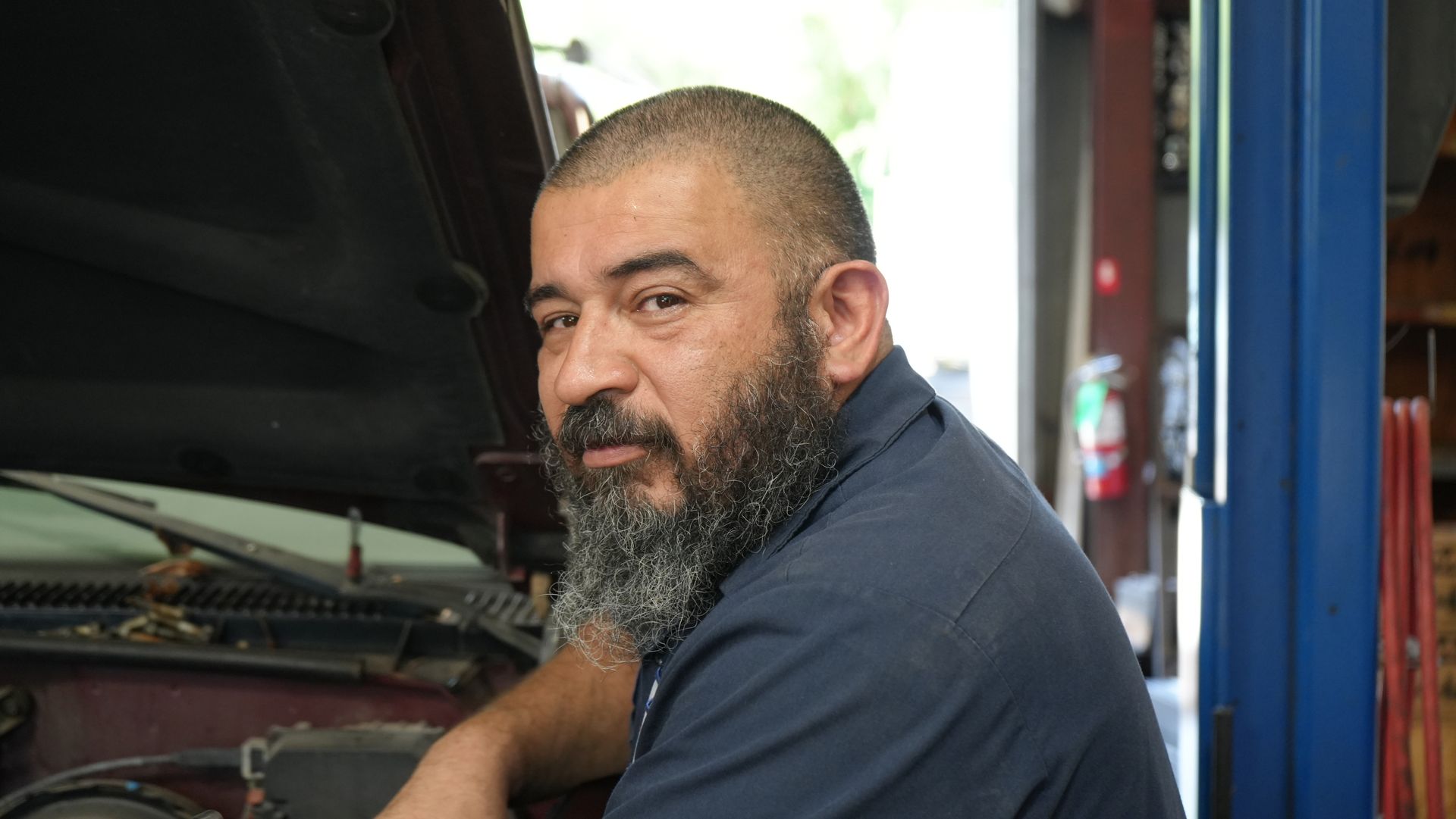 A man with a beard is working on a car in a garage.