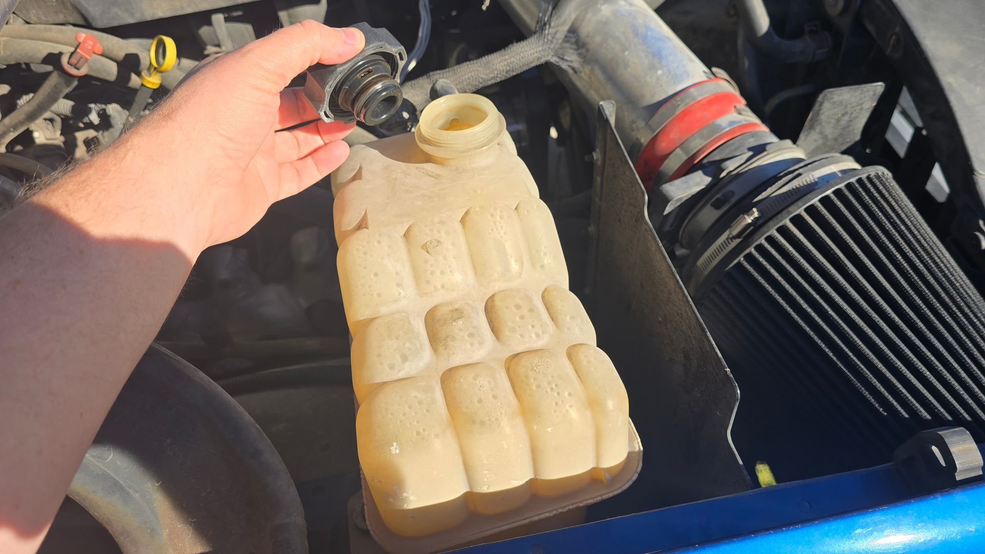 A person is pouring water from a bottle into a car engine.