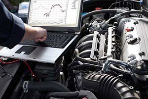 a man is working on a car engine with a laptop .