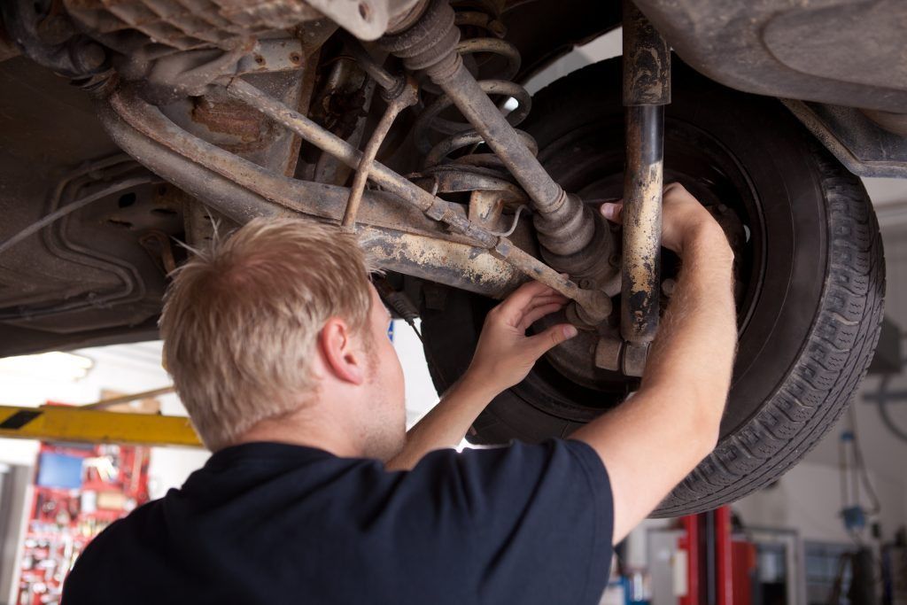 a man is working on the underside of a car in a garage .