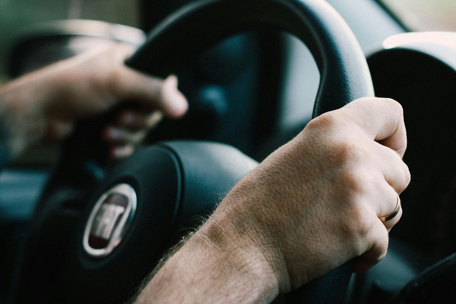 Hands gripping a car steering wheel; interior view, blurred background.