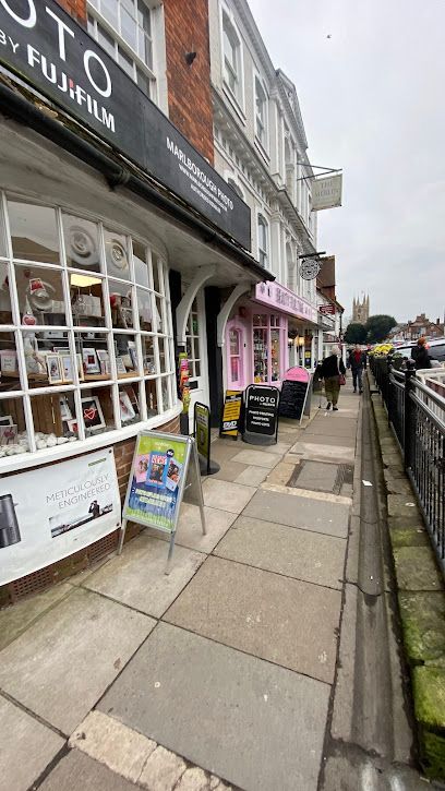 Street view of shops with awnings, sidewalk, and parked cars on a cloudy day.