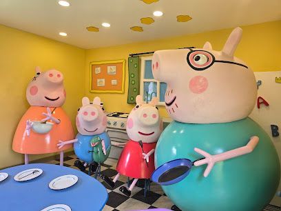 Peppa Pig family in a kitchen: yellow walls, blue table with plates, Papa Pig holding pan, and smiling.