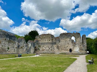 Ruined stone castle walls under a blue sky with fluffy clouds. Green grass and walking path in foreground.