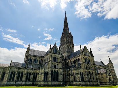 Salisbury Cathedral with a tall spire under a blue sky with clouds.