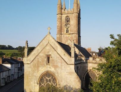 Stone church with tower, arched windows, cross on top, against a blue sky.