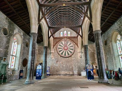 Great Hall interior with large Round Table replica, stone walls, wooden beams, stained glass windows.