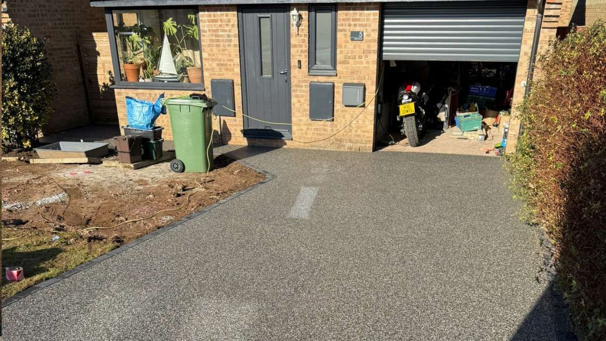 Driveway with a green trash can, a garage with a motorcycle, and a brick house.