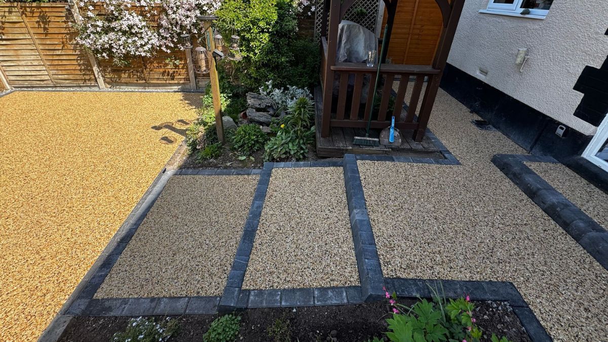 A gravel pathway bordered by dark gray edging, leading to a small wooden shed.