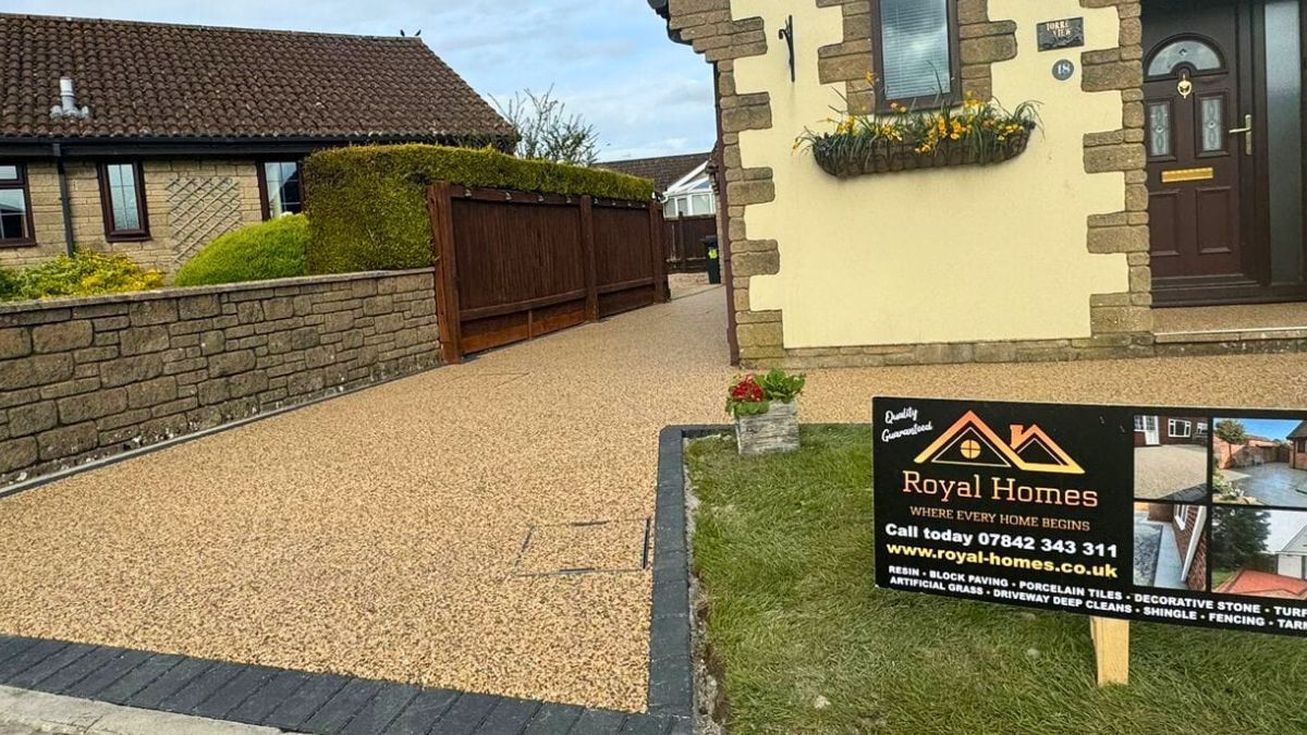 A house with resin driveway, brown fence, and real estate sign on the front lawn.