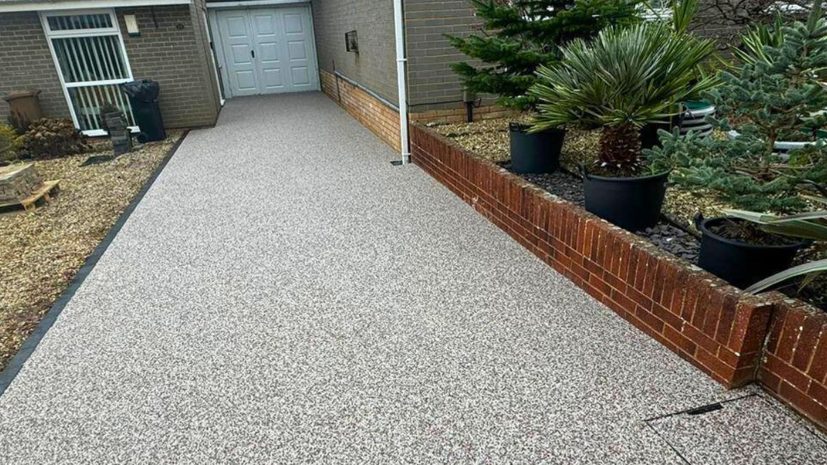 Resin bound driveway with light gravel, next to a low brick wall with potted plants.