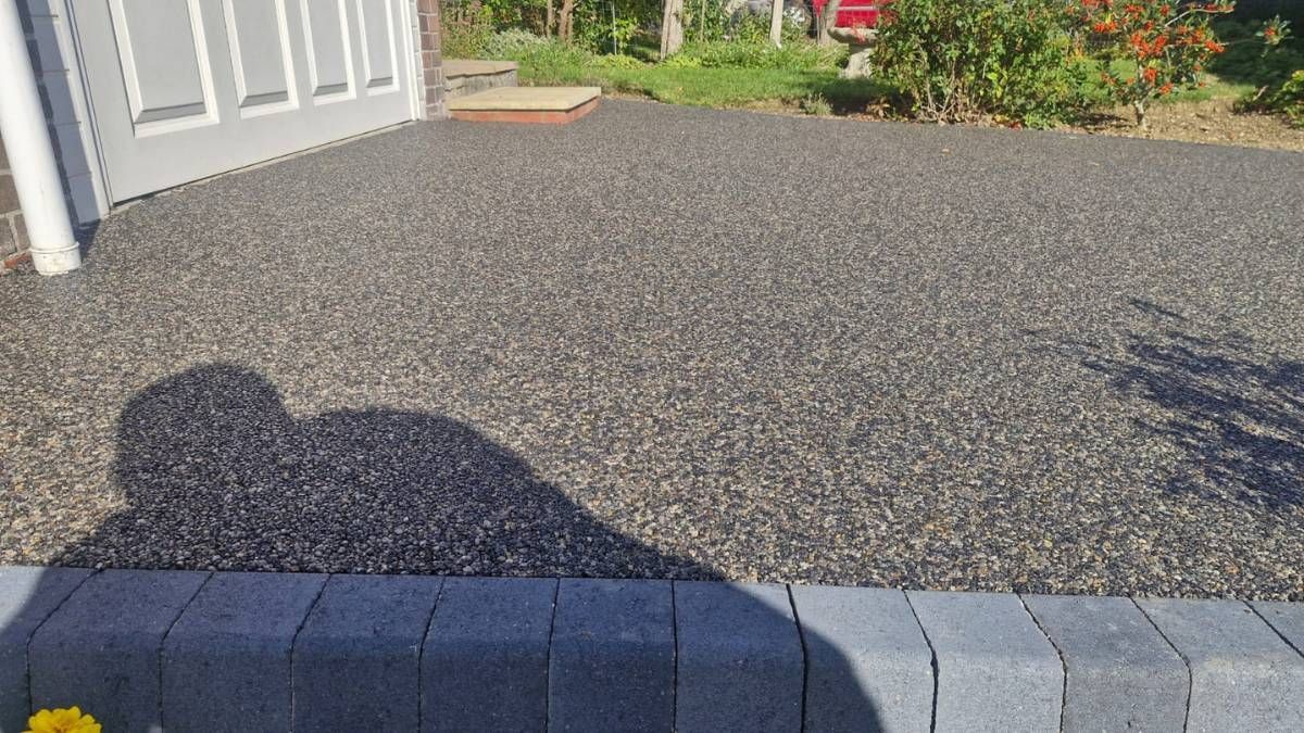 Shadow on a gravel driveway with a border of gray bricks, next to a building with white doors.
