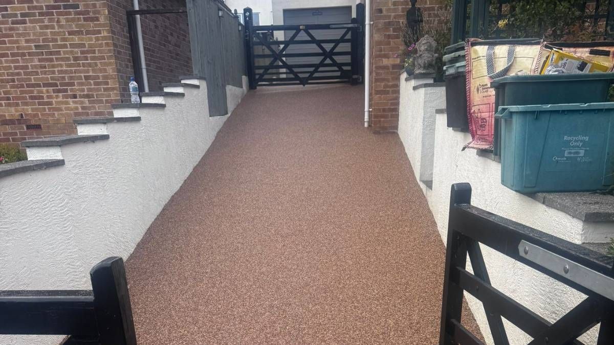 Driveway with brown gravel, black gate, white walls, steps, and green trash bin.
