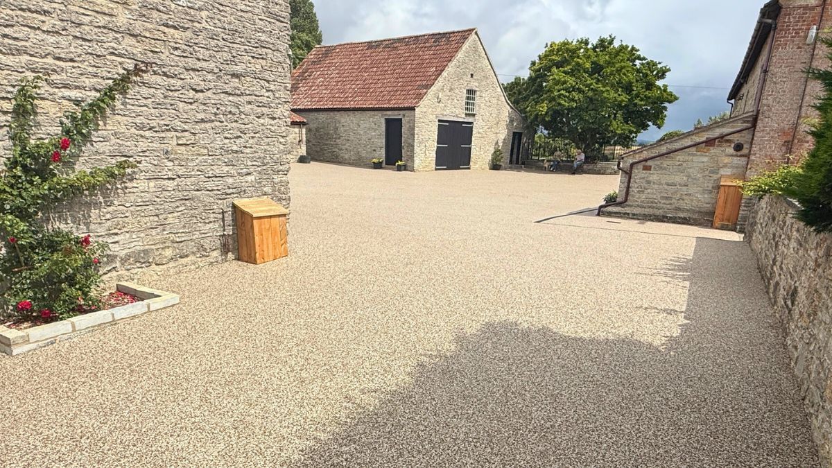 Stone buildings and resin courtyard with a red-roofed barn under a cloudy sky.