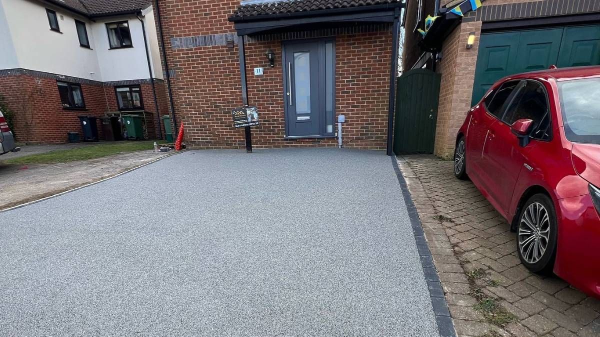 Red car parked next to a driveway made of gray gravel, leading to a brick house.