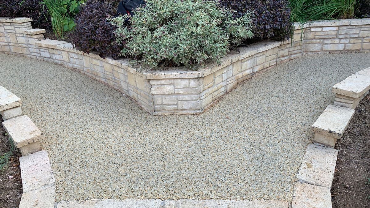White resin paths split into two around a raised flowerbed, bordered by light-coloured stone walls.