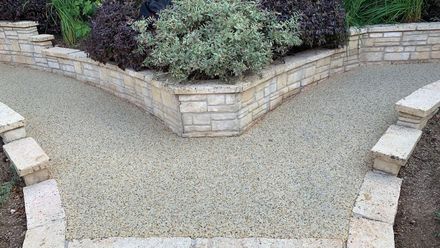 White resin paths split into two around a raised flowerbed, bordered by light-coloured stone walls.