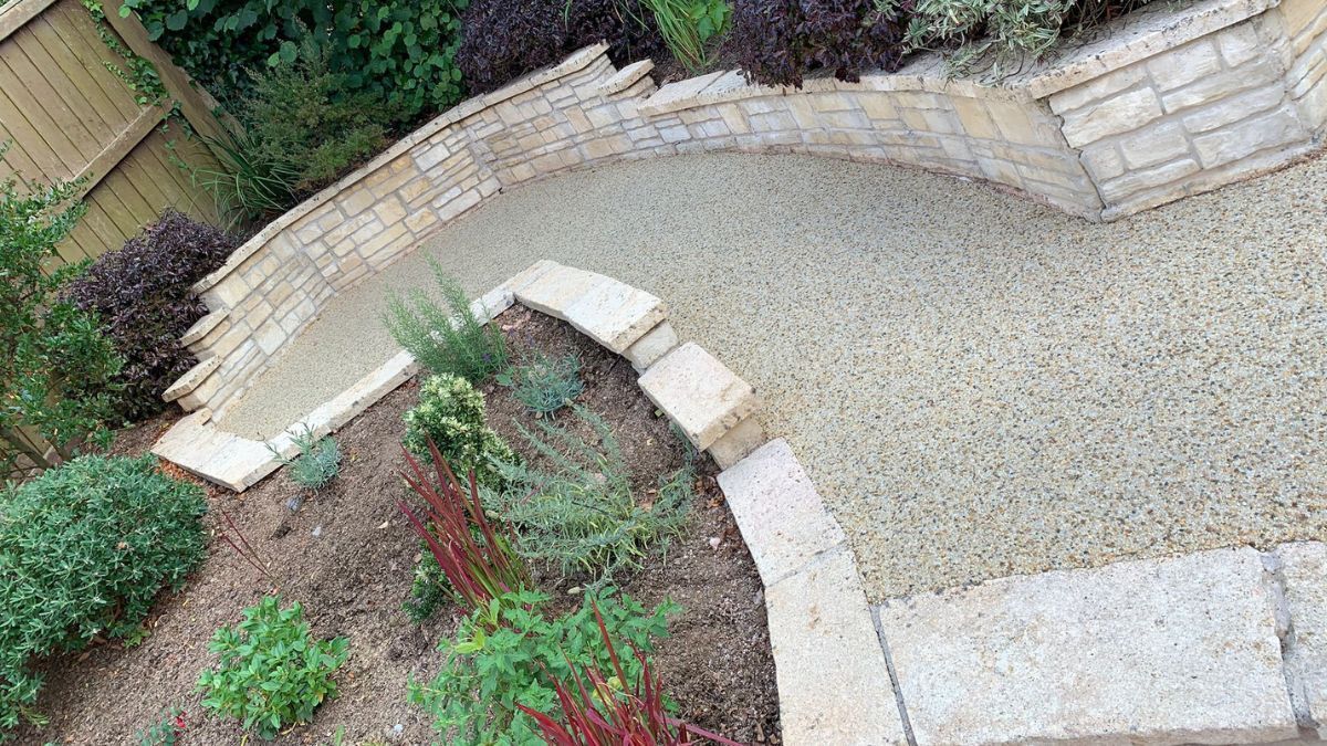 Stone pathway winding through a garden, bordered by a stone wall and landscaping.