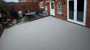 A gray resin patio with a table, chairs, and access to a house with a white door and windows.