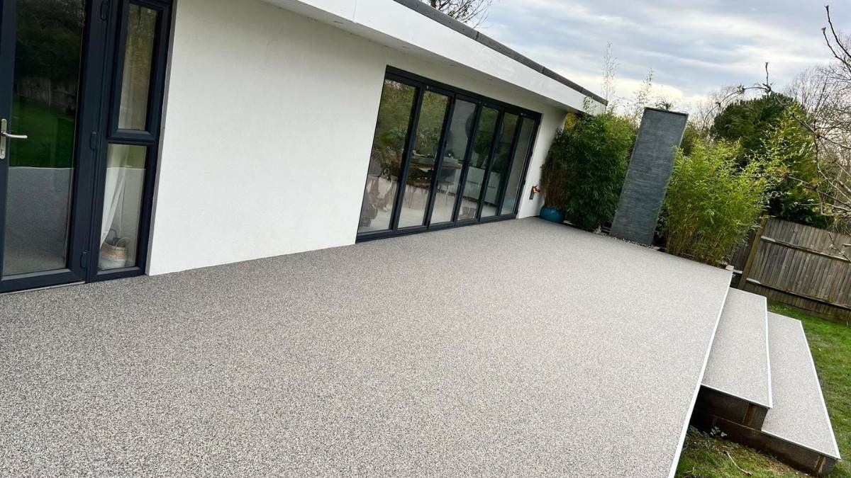 Exterior view of a house with a gray speckled resin patio and steps leading to a green lawn.