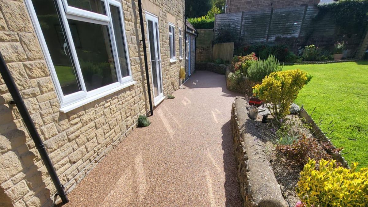 A paved patio alongside a stone-walled house with a garden bed and lawn.