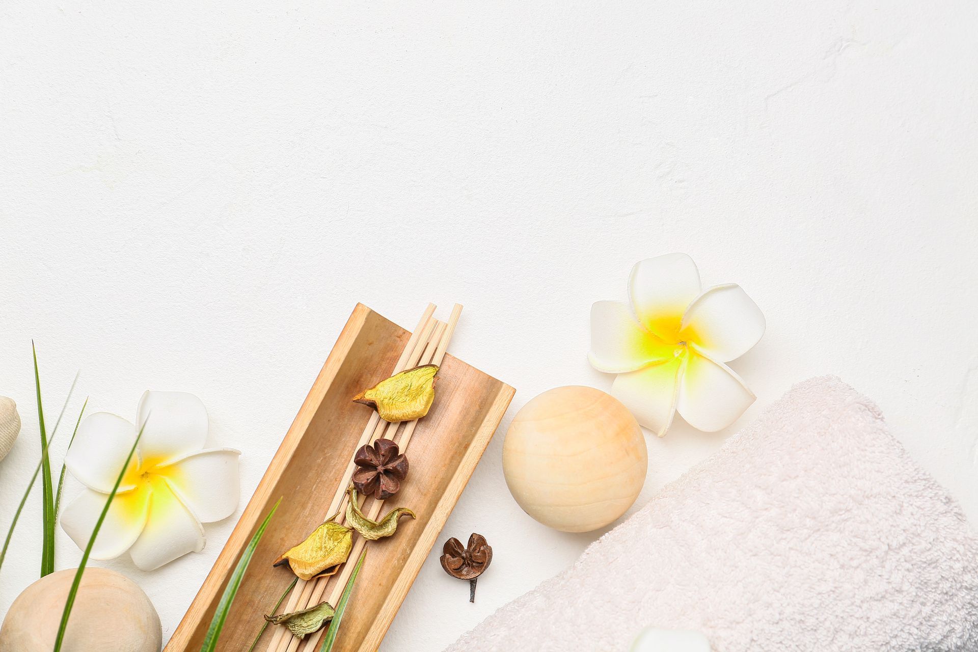 Spa arrangement: white towel, flowers, bamboo tray with potpourri, on white surface.