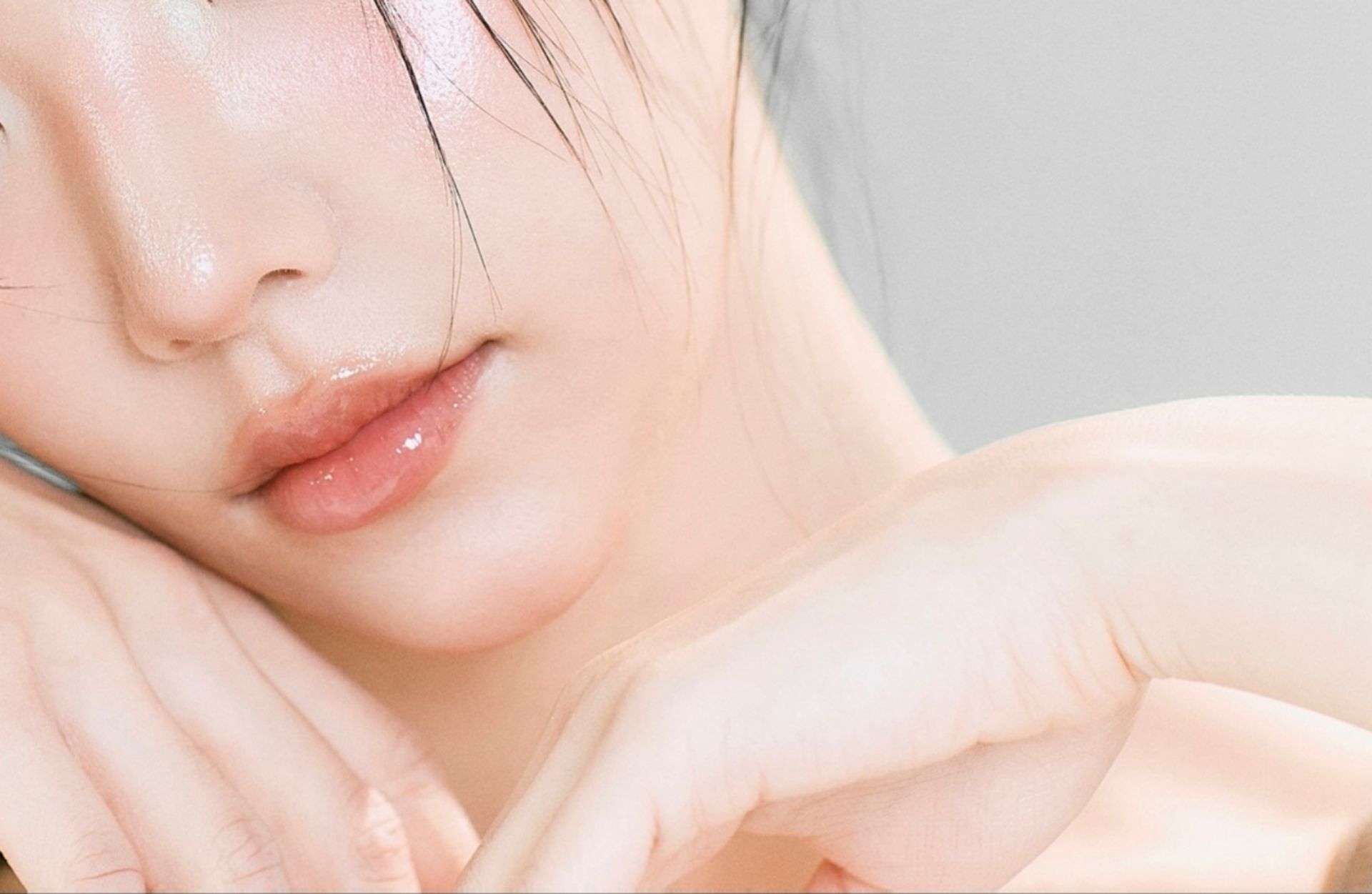 Close-up of a person's face. Shiny, plump lips and soft skin; the person is leaning on their arms.