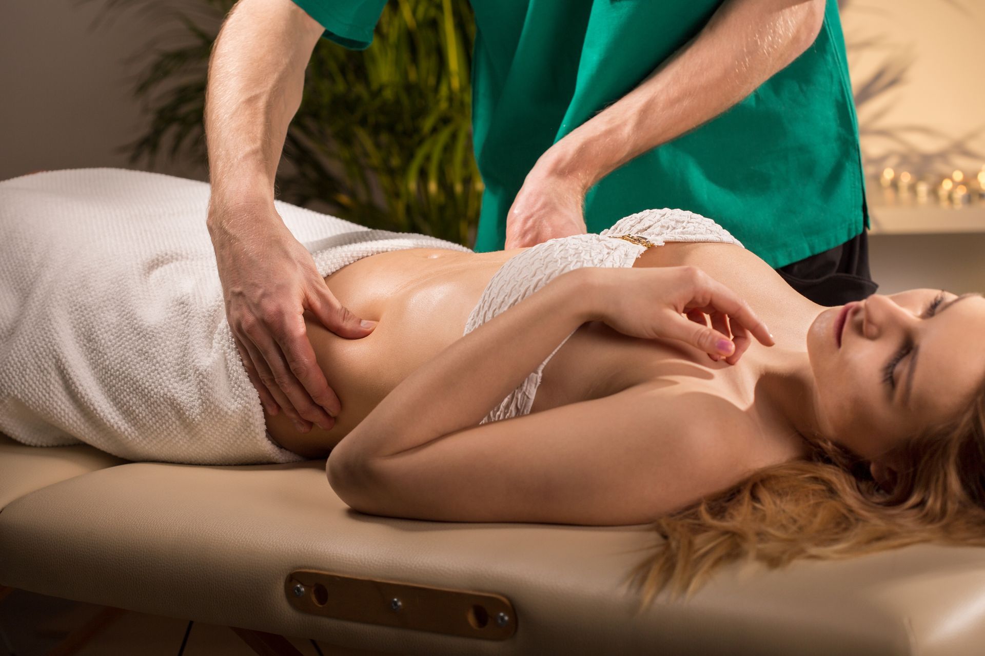 Woman receiving abdominal massage, lying on a massage table, with a therapist in green scrubs.