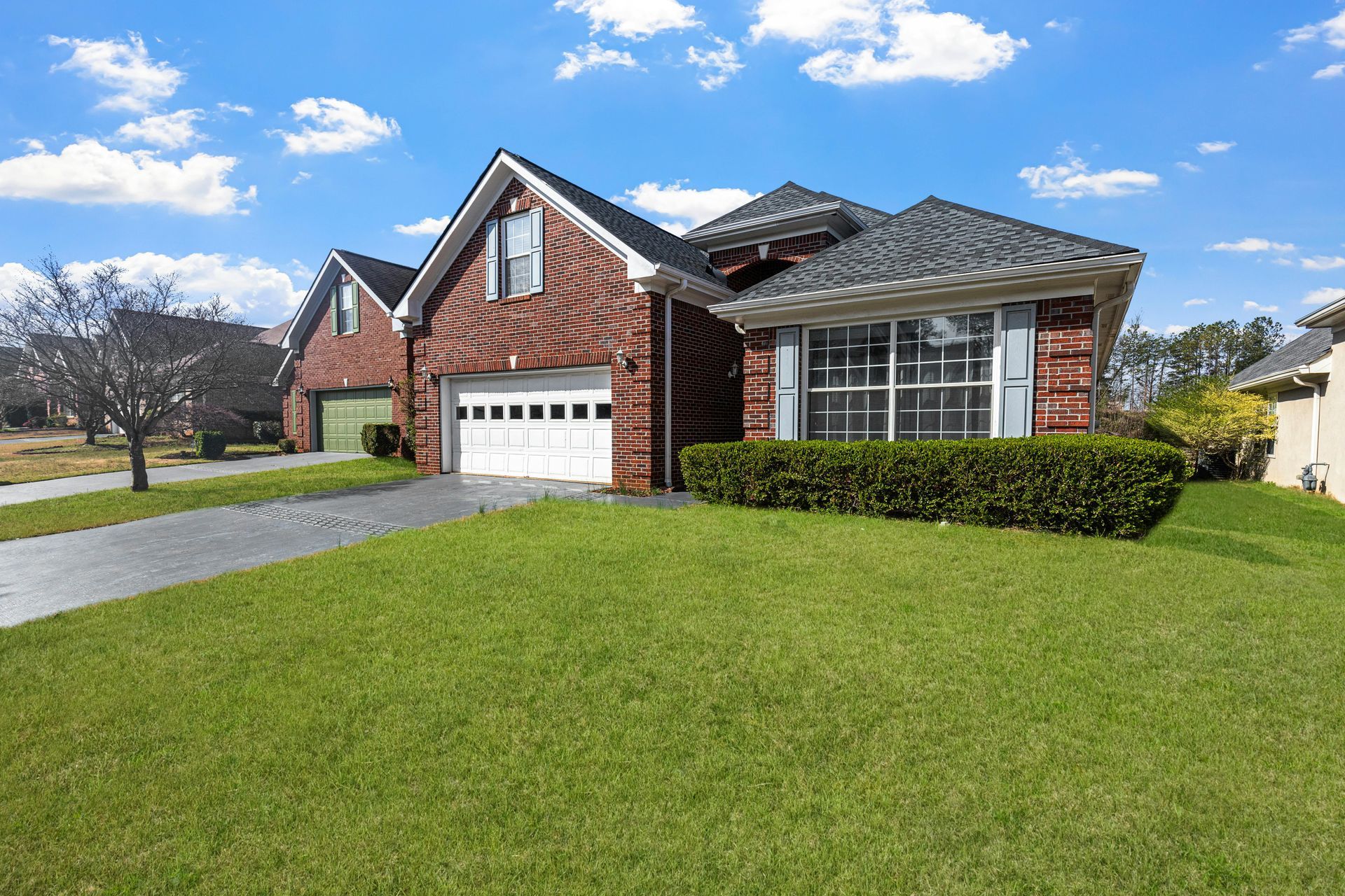 Suburban brick house with white garage, large front lawn, and clear blue sky