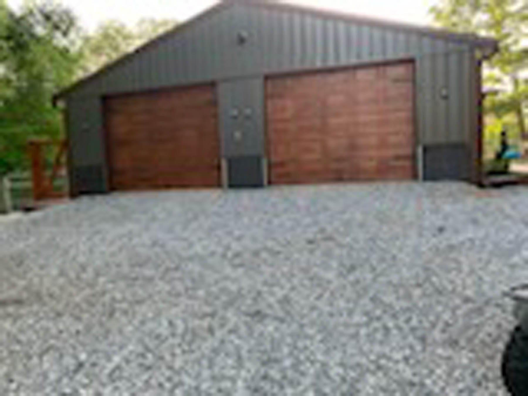 Two-bay garage with brown doors and gray corrugated metal siding, gravel driveway.