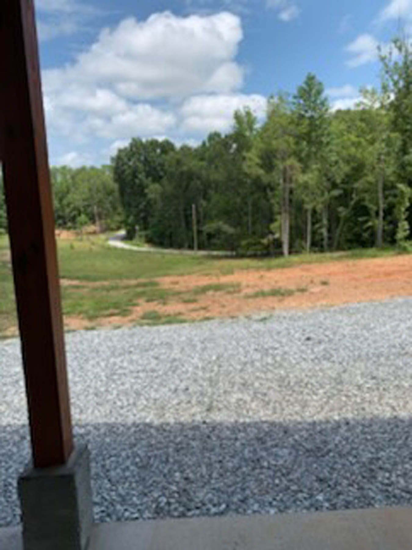 Gravel driveway with a view of a dirt road through a clearing surrounded by green trees under a partly cloudy sky.