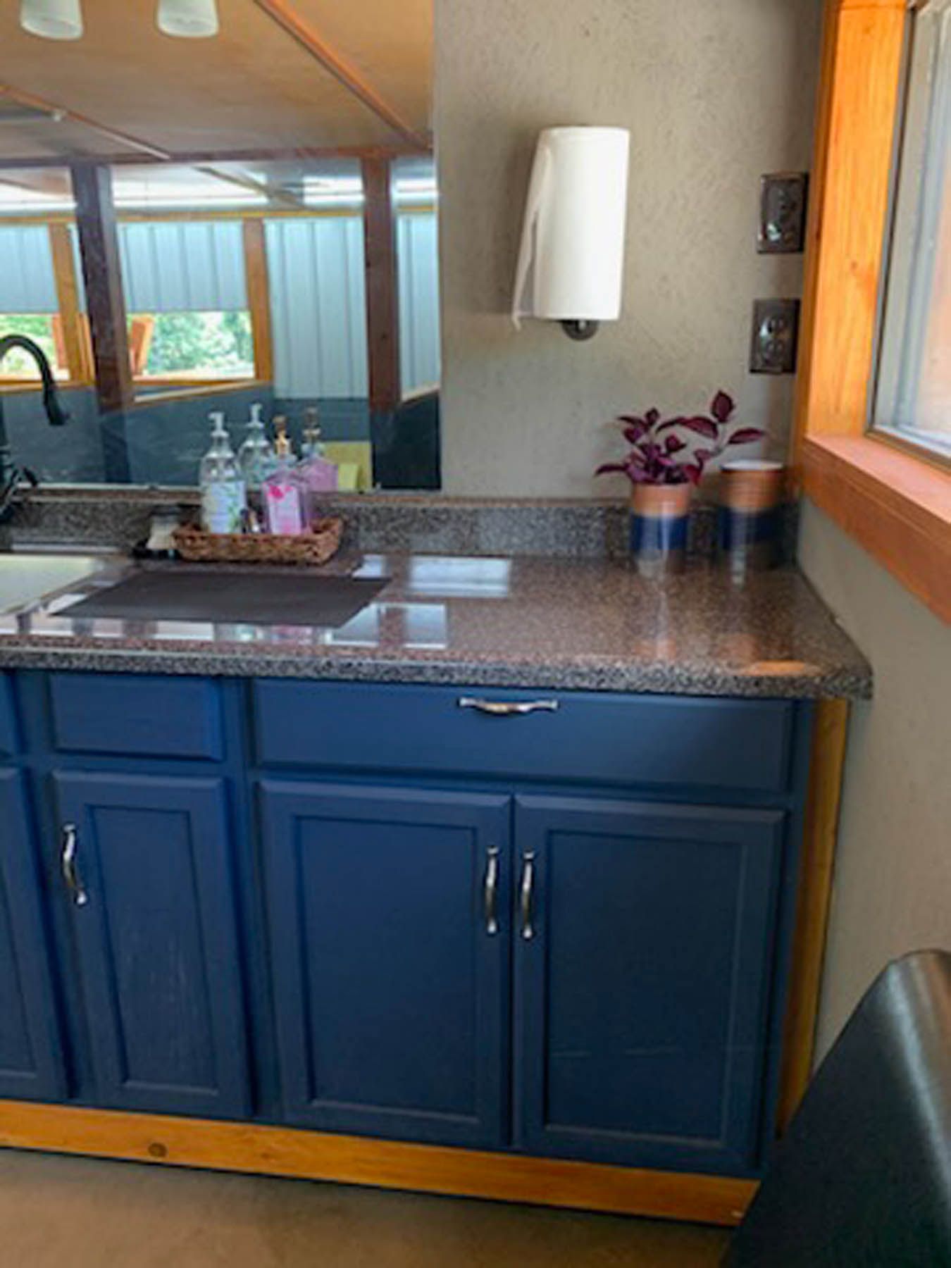 Blue cabinets under a countertop with a sink. A paper towel holder, copper pots and a plant are on the countertop.