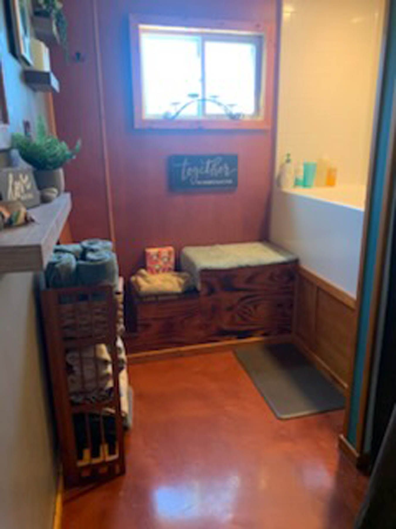 Small bathroom with red floor, wooden details, towels, and a window.