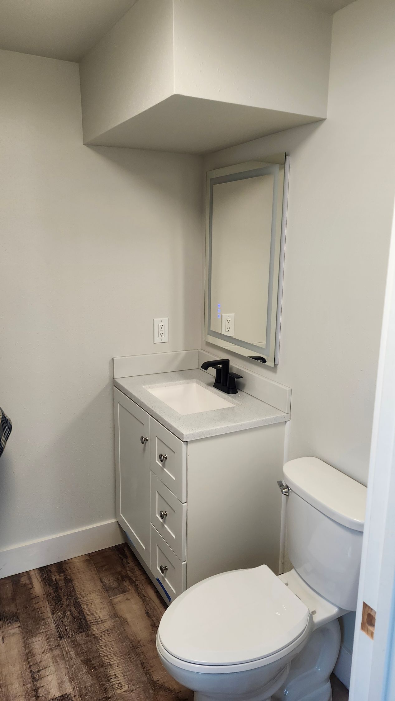 Bathroom with white vanity, toilet, and mirror, gray walls, and wood-look flooring.