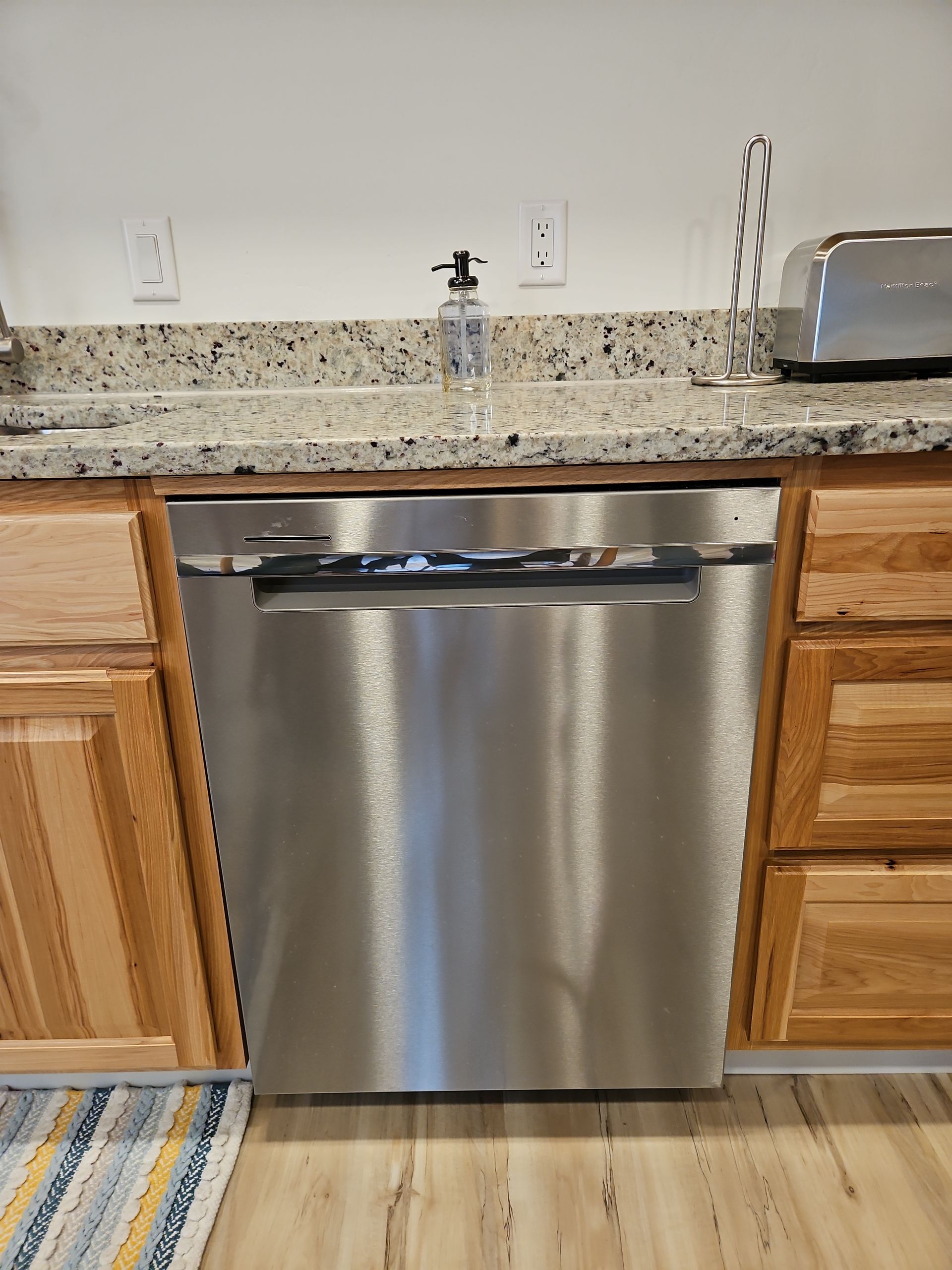 Stainless steel dishwasher in a kitchen with wood cabinets and a granite countertop.