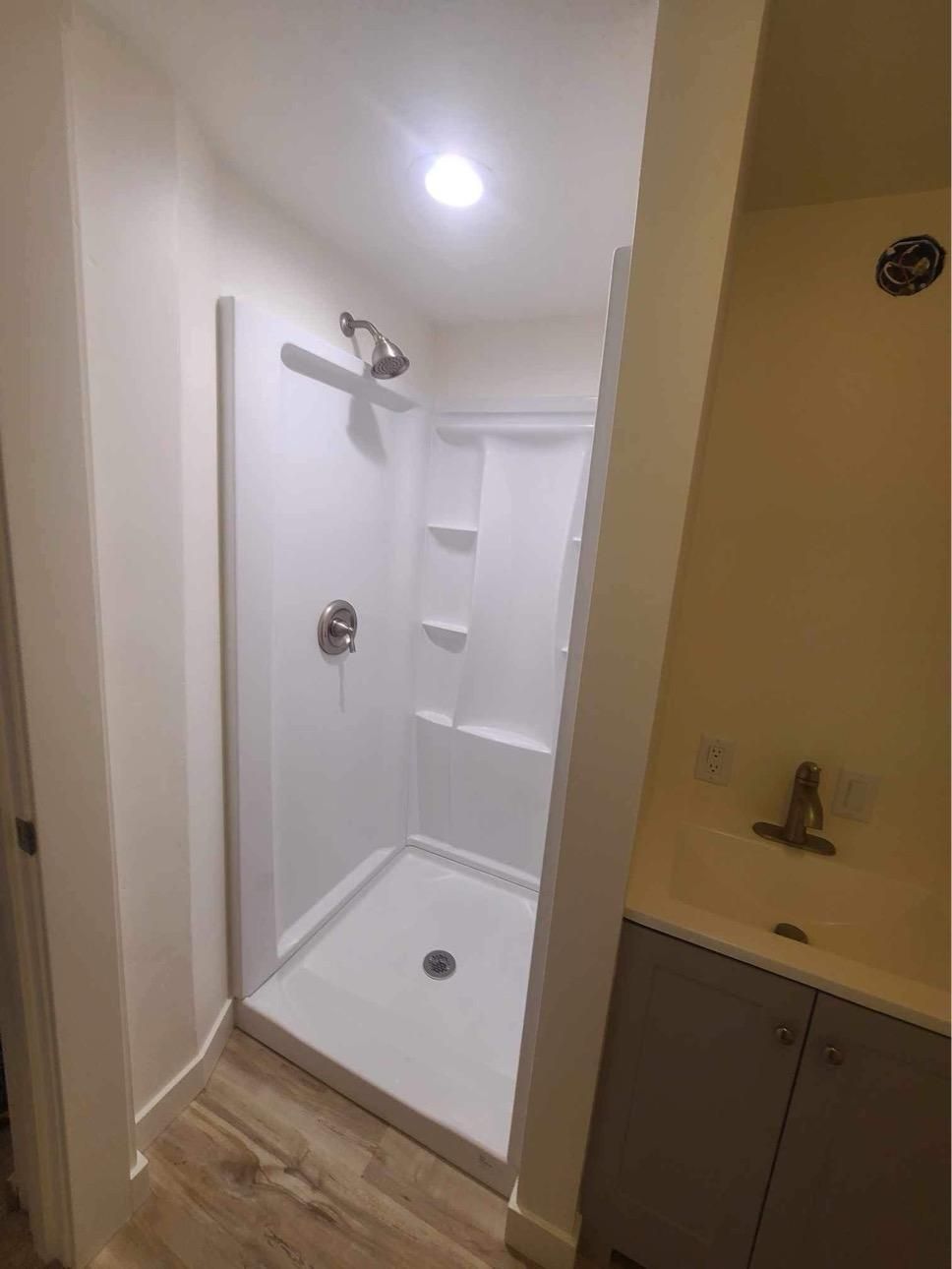 White shower stall with silver fixtures and a sink in a small bathroom.