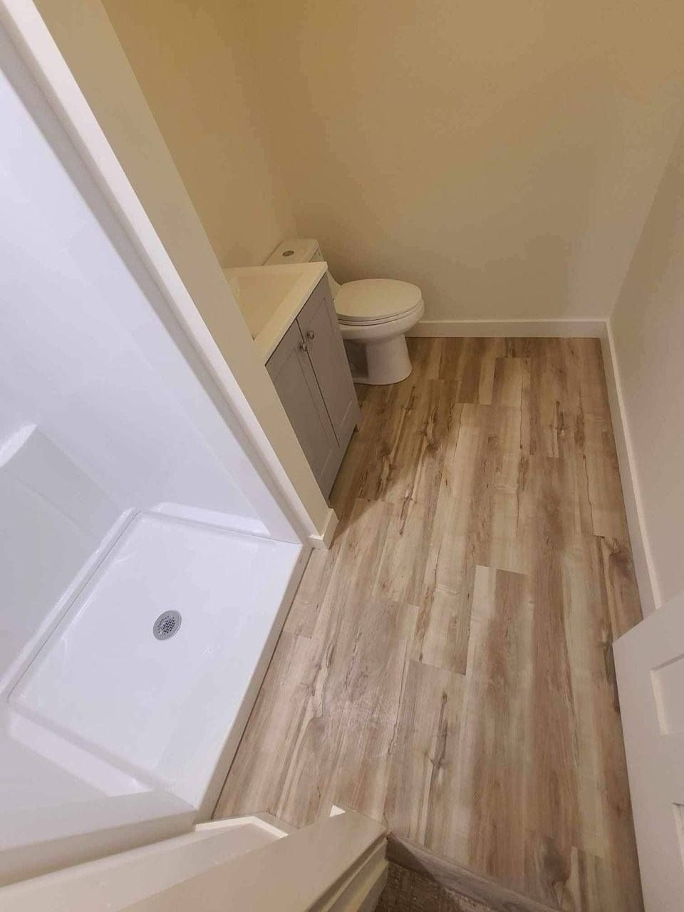 Small bathroom with a shower, toilet, and vanity cabinet. Wood-look flooring and light walls.