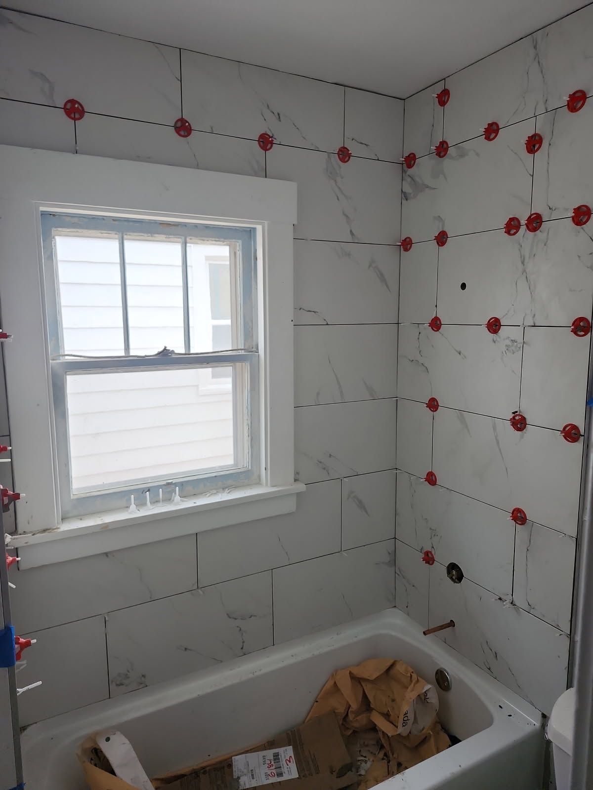 Bathroom with white tiles, window, and a bathtub; red tile leveling system used.