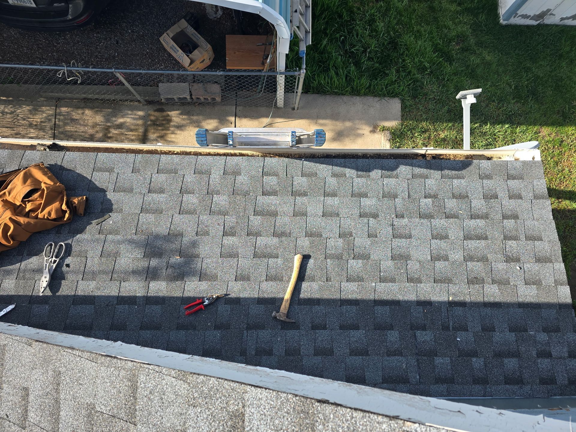 A partially shingled roof with tools (hammer, pliers) and a brown bag.