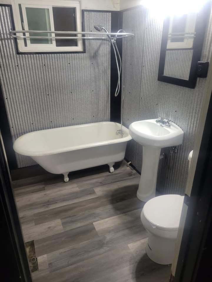 Bathroom with a clawfoot tub, pedestal sink, and toilet, gray wood-look floor, and corrugated metal wall.