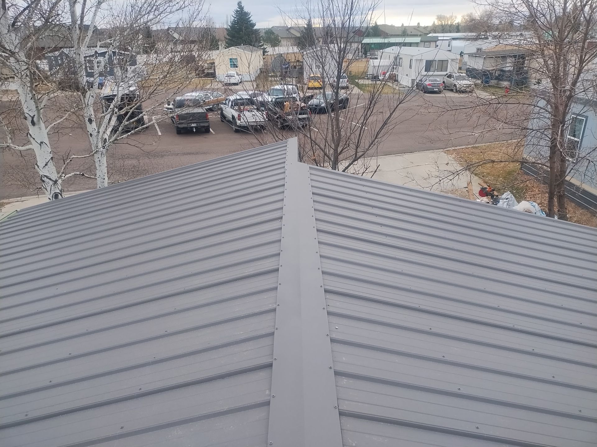 Gray metal roof with a central ridge, looking over a parking lot and buildings.