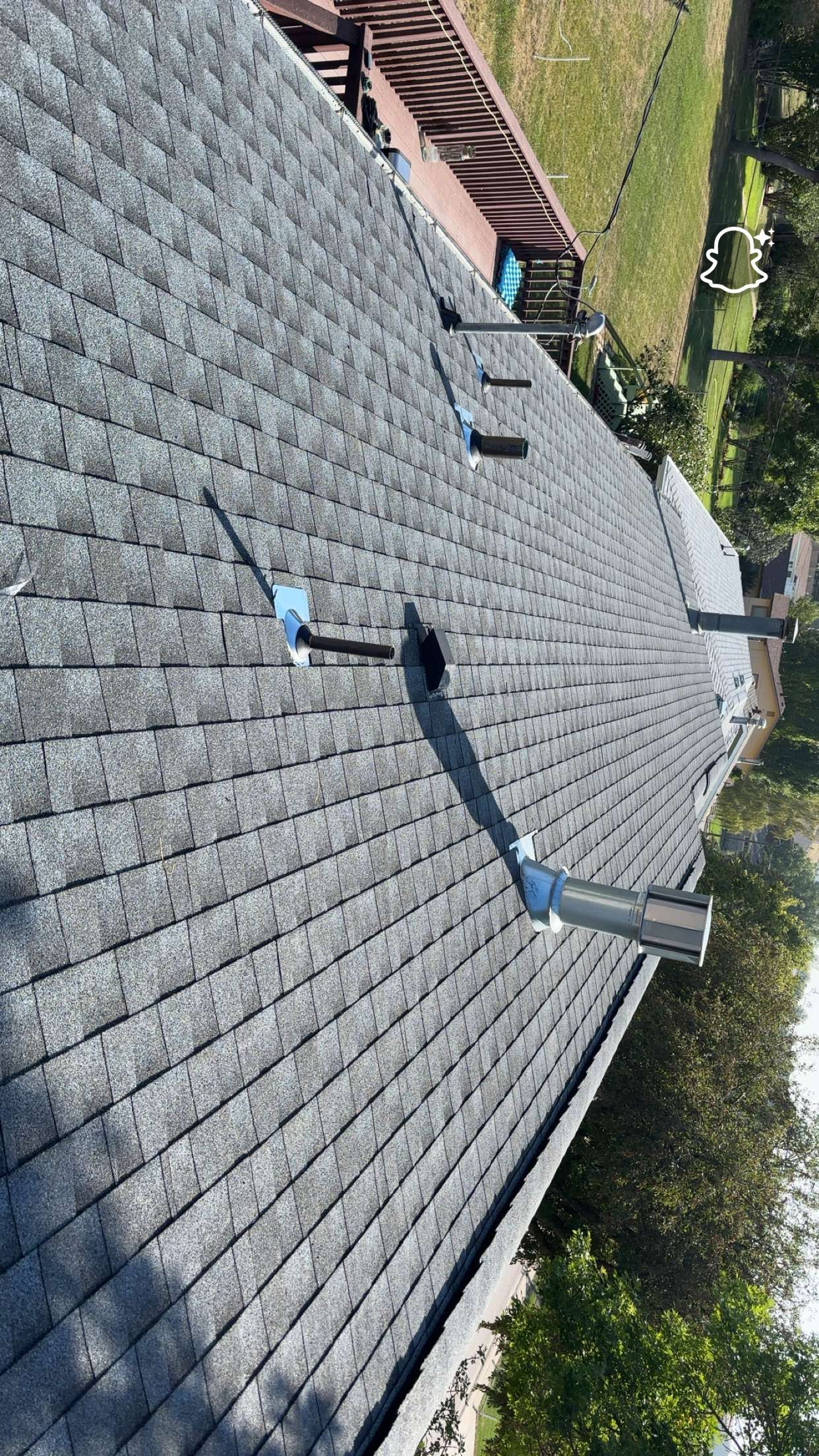 Gray asphalt shingle roof with vent pipes extending upwards. Outdoors.