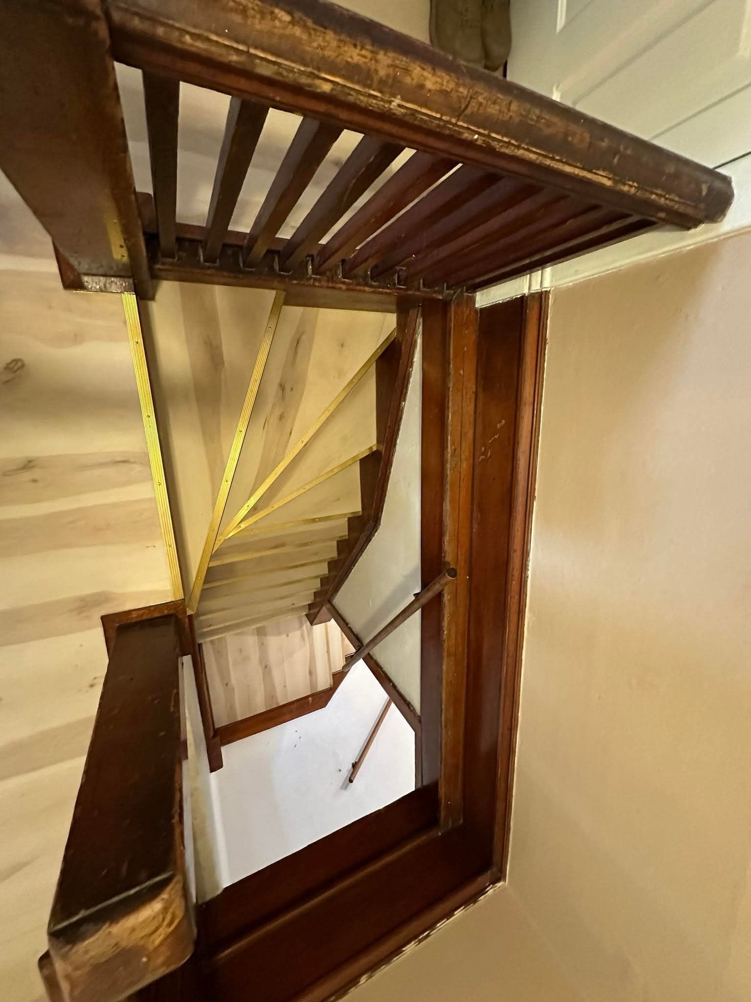 Wooden staircase viewed from above. Brown handrails, light-colored stairs, and a decorative wooden ceiling detail.