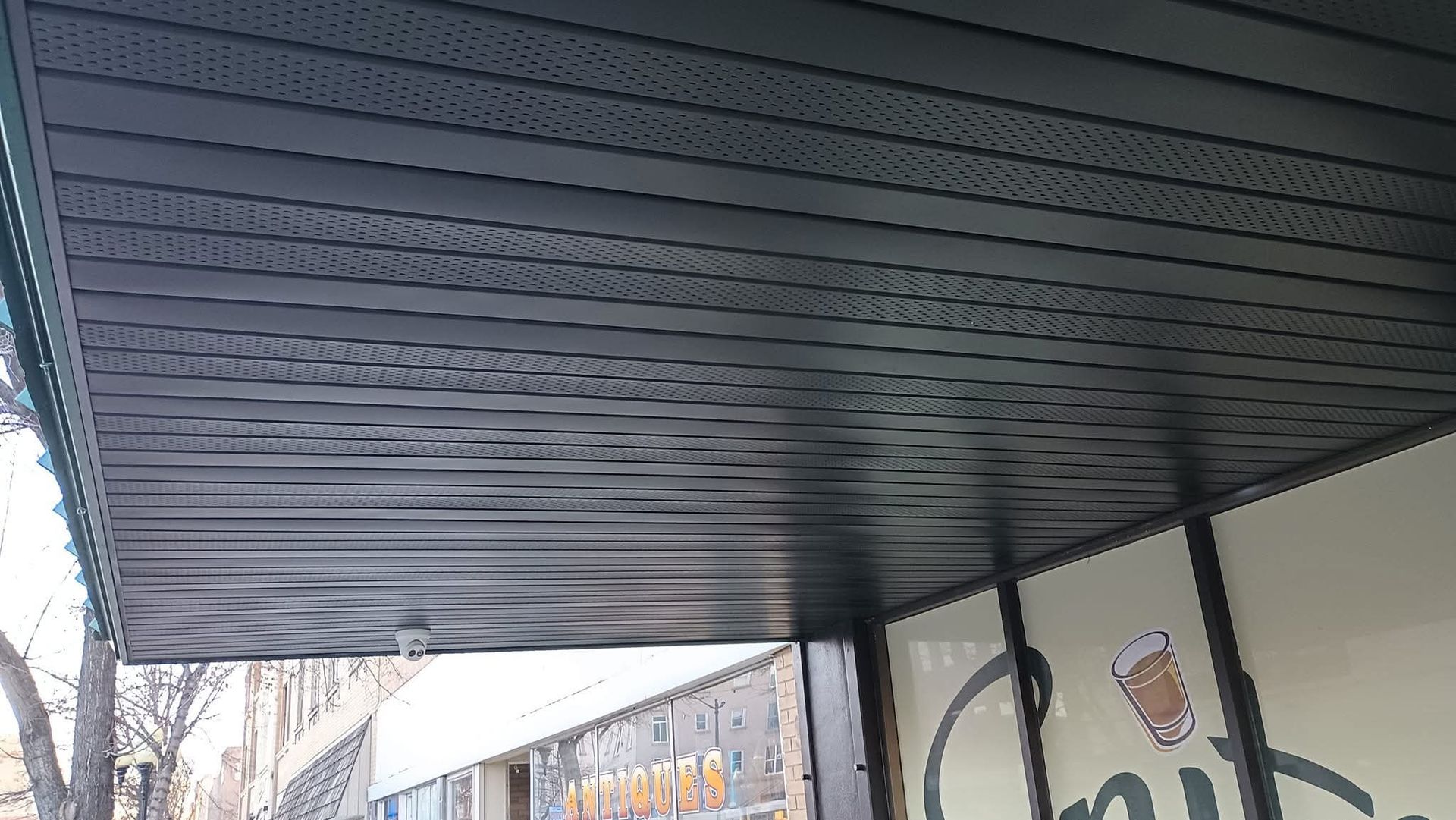 Black awning over a business entrance with horizontal lines and perforated pattern.