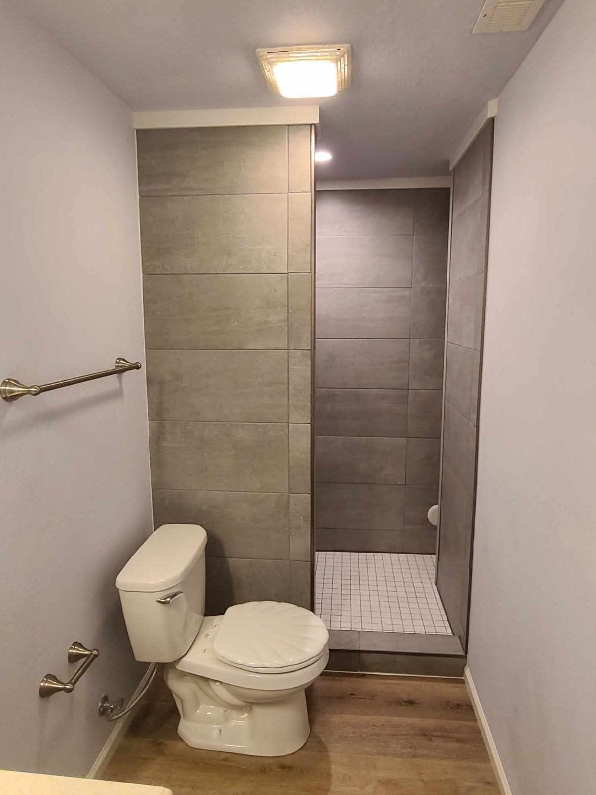 Small bathroom with gray tile shower, toilet, and towel rack.